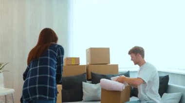 Happy young Caucasian couple unpacking their stuff from cardboard boxes in new house. Relocation concept, boyfriend and girlfriend moving in together. Spouses unpack in new apartment. Married life