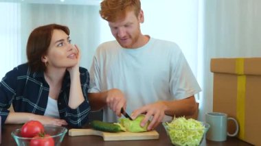 Camera moving back from young happy family couple preparing food together in new home. Beautiful woman and handsome man cooking in own flat. Spouses at home in good mood. Romantic relations concept