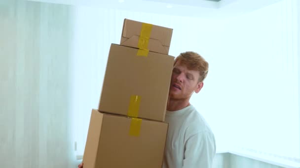 接近一个英俊的白种人红头发的男人 手里拿着许多纸盒在屋里 箱子掉在地板上了 搬迁的概念 搬出公寓 换了家实时 — 图库视频影像
