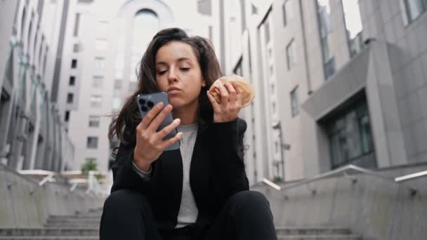 Genç Güzel Bir Kadın Merdivenlerde Oturuyor Hamburger Yiyor Akıllı Telefonunu — Stok video