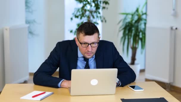 黒いスーツの男と青いシャツを着た男がテーブルに座り コンピューターを操作している オフィスで働いている白人男性がノートパソコンに入力して画面を注意深く見て回ります — ストック動画