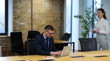 Orta yaşlı, beyaz bir adam laptopuyla ofisinde çalışıyor. Kadın ofise geliyor ve masasına siyah maaşlı beyaz bir zarf koyuyor. Adam zarfa bakar, parayı kontrol eder ve mutlu görünür..