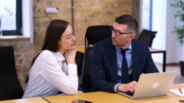 Beyaz adam ve kadın modern ofiste masanın üzerinde oturuyorlar. Beyaz gömlekli bir iş kadını erkek meslektaşına fikirlerini açıklıyor. Mavi gömlekli ve siyah takım elbiseli adam mutlu görünüyor, gülümsüyor..
