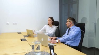 Beyaz tenli işadamı ve işkadını ahşap masadaki beyaz ofiste oturuyor ve konuşuyorlar, başka bir adam odaya giriyor, ve o oturuyor. Erkek, iş görüşmesi için büyük bir şirkete geldi..