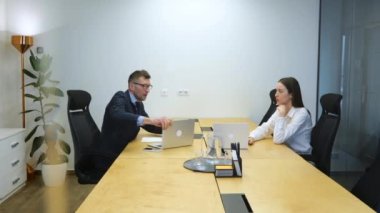 Beyaz adam ve kadın ofis alanında beyaz çağdaş ofis alanındaki büyük ahşap masada oturuyorlar ve işadamları iş kadınlarıyla tartışıyor. Erkek odayı terk etti ve kadın üzgün görünüyor..