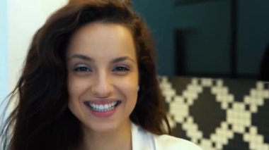 Kamera, mutfakta durup kameraya gülümseyen güzel, neşeli genç bayandan geriye doğru hareket ediyor. Kapatın. Kafkasyalı seksi esmer kadın modern dairede kameraya bakarak gülümsüyor. Gerçek zamanlı..