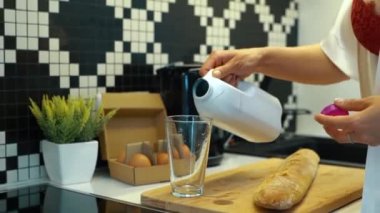 Kafkasyalı, bornozlu, iç çamaşırlı, elinde şişe olan ve evdeki mutfakta bir bardağa süt döken güzel bir kadın. İç çamaşırlı kadın kahvaltı hazırlıyor. - Günaydın. Gerçek zamanlı. Yemek pişirme