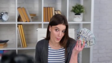 Beyaz bir bayan evdeki kamerasında bir sürü para gösteriyor. Canlı yayın yapan kadın, takipçilere dolar banknotları gösteriyor. Yavaş çekim videosu