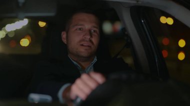 Geceleri araba süren ve gülümseyen neşeli, beyaz, yakışıklı iş adamına yaklaş. Takım elbiseli mutlu adam akşam iş yerinden arabayla geliyor. Taksi şoförlüğü. Trafik, gezi. Yavaş çekim konsepti