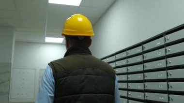 Sarı miğferli işçi erkek ustabaşının inşaat alanını teftiş edişinin arka görüntüsü. İnşaat işçisi inşaat alanında çelik yelek ve şapka takıyor. Gerçek zamanlı.