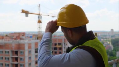 Mühendis inşaat alanının çatısında dinlenirken başlığını çıkarıp saçına dokunuyor. Mühendislik ve mimari kavramı