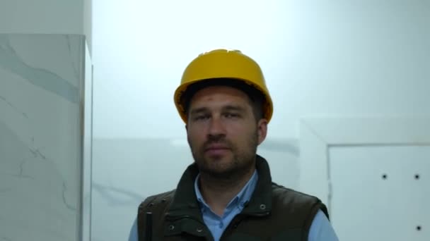 黄色のハードハット歩くと建物の建設現場を検査する幸せな男性のフォアマン 建物に沿って歩く建築家 工事の施工者コンセプト — ストック動画