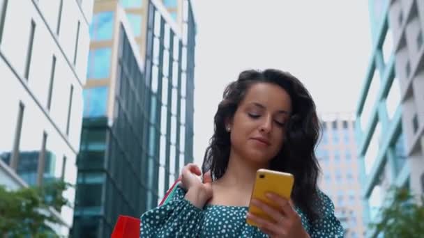 Sokakta Yürürken Alışveriş Torbaları Taşıyan Mutlu Bir Kadın Cep Telefonu — Stok video