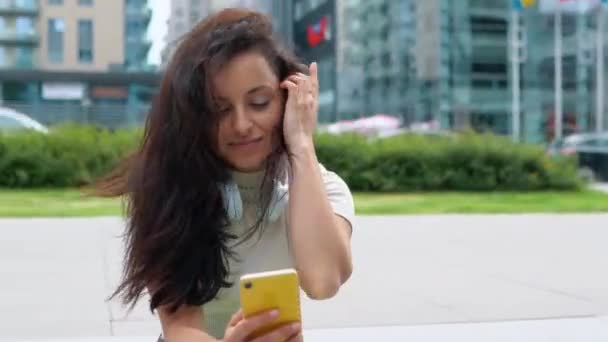 一边看短信一边笑着拿着手机的年轻女士 女士在户外的台阶上坐着时使用智能手机 生活方式的概念 — 图库视频影像