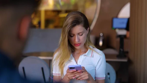 Upset lady using smartphone and reading message while having dating. Young woman is nervous and looking away while sitting in front of her boyfriend. Real time