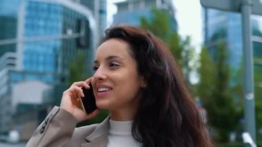 Şehirde sokakta yürürken cep telefonuyla konuşan mutlu çekici bir iş kadını. Akıllı telefon kullanan bir bayan. Gerçek zamanlı.