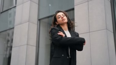 Ofis binasının önünde caddede duran genç ve güzel bir iş kadını. Dışarıdaki kameraya poz veren bayan girişimci. Yaşam tarzı, iş, iş konsepti. Gerçek zamanlı.