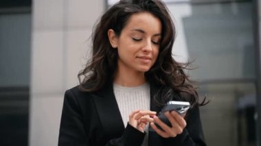 Cep telefonuyla çalışan mutlu bir bayan. Gülümseyen bayan dışarıda duruyor ve telefon ekranında sallanıyor. Teknoloji, dijital konsept. Gerçek zamanlı.