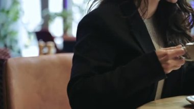 Kahve içerken cep telefonu tutan ve kullanan bir kadın. Bir kadın akıllı telefondan mesaj atarken kahvecide yemek yiyor. Yaşam tarzı konsepti. Gerçek zamanlı.