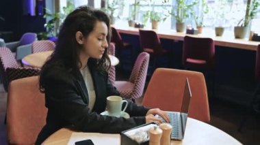 Kafeteryada naneli çay içip dizüstü bilgisayar kullanan beyaz bir kadın. Mutlu gülümseyen kadın çalışıyor, dizüstü bilgisayardan mesaj atıyor. Serbest çalışan, internette çalışan, internette gezinen. Teknoloji konsepti. Gerçek zamanlı.