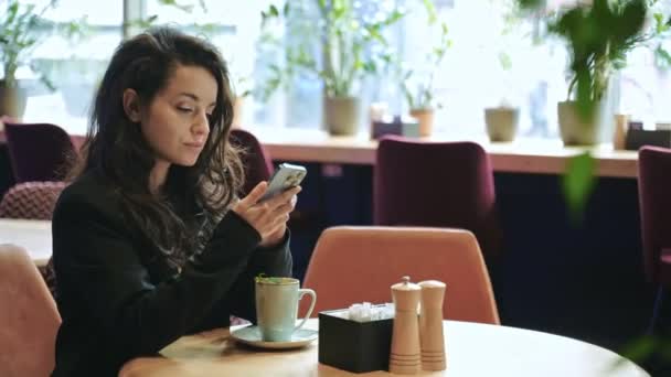 快乐美丽的女士在咖啡馆休息 同时使用智能手机 笑漂亮的女人在手机上打字和喝薄荷茶 生活方式的概念 — 图库视频影像