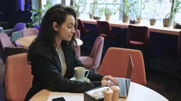 年轻的高加索女人在咖啡店喝薄荷茶和使用笔记本电脑 快乐地微笑着工作的女性 在笔记本电脑上发短信 自由职业者 在网上工作 浏览互联网 技术概念 — 图库视频影像
