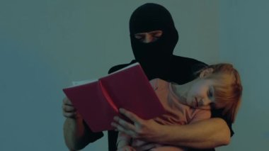 Küçük bir kız rehine için kitap okurken kaçırılan bir erkek. Suçlunun ellerinde uyuyan küçük kız. Uzayı kopyala Çocuk kaçırma konsepti. Yavaş çekim