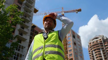 Beyaz, mutlu, yakışıklı, profesyonel bir inşaatçı güneşli bir günde sarı kaskını çıkarıyor. Kapatın. Alt manzara. İnşaat işi, mimarlık endüstrisi, mühendislik işi.