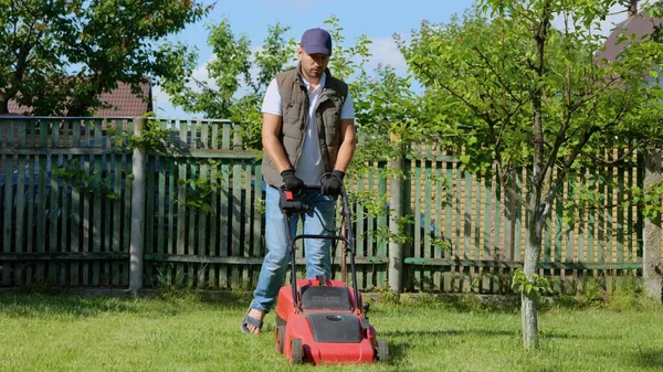 잘생긴 정원사가 잔디깎는 기계로 잔디를 여름날 청년은 정원에서 아름다운 디자인 — 스톡 사진