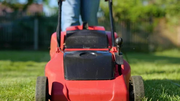 Close up shot of lawn-mower cutting green grass outdoor in garden. Man mows lawn in the backyard with electric lawn mower. Slow motion. Male worker walking in yard using lawn mower. Gardening concept