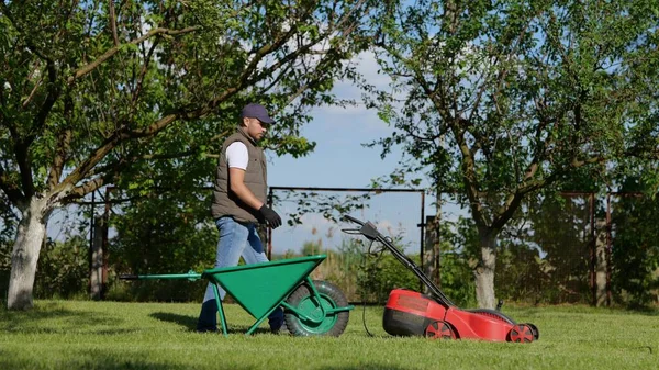 Young Caucasian Man Unload Grass Lawn Cutter Machine Bag Wheelbarrow — 스톡 사진