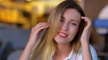 Close up of beautiful cheerful blonde female sitting in restaurant and flirting talking to camera. Caucasian happy pretty young woman on a date looking at camera smiling and speaking. Flirt concept