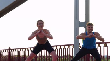 Cheerful positive man and woman in sportswear working out together outdoors doing side lunges. Caucasian sportsman and sportswoman couple doing exercise on glutes. Physical activity. Sport concept
