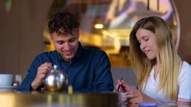 Close up of Caucasian joyful young man and woman smiling and eating in restaurant indoors. Cheerful couple boyfriend and girlfriend sitting in cafeteria on a romantic date. Love. Dating. Slow motion