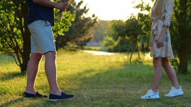 Romantic date in park. Caucasian handsome happy male giving flowers to young beautiful woman outdoors. Summer weekend on nature. Love relationships. Girlfriend hugging beloved boyfriend. Slow motion