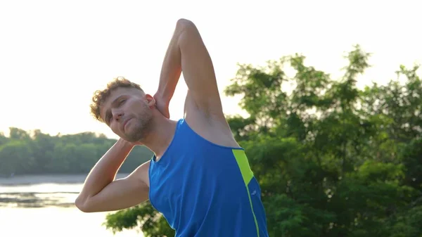 Close up of handsome curly man athlete doing exercise outdoor stretching muscles. Young sportsman in sportswear warming up his body before workout. Sport activity. Healthy lifestyle concept