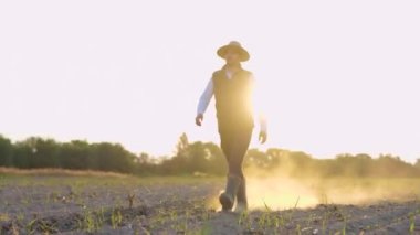 Lastik çizmelerle tarlada yürüyen hasır şapkalı mutlu bir sahibi. Organik gıda, toprak bereketi, ekoloji, tarım sektörü konsepti. Gerçek zamanlı.