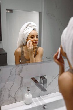 Mutlu genç bir kadın banyoda durup yüzünü süngerle temizlerken sabah hazırlıkları yapıyor. Güzellik ve Tedavi konsepti