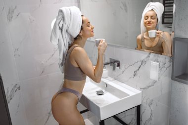 Mutlu kadın evde kahvesini yudumlarken, banyoda dikilip aynaya bakarken rahatlıyor. İç çamaşırlı kadın.