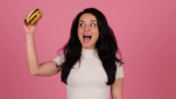 Sorrindo Bela Fêmea Vai Comer Hambúrguer Enquanto Posando Fundo Rosa — Vídeo de Stock