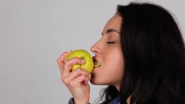 Gri arka planda izole edilmiş taze elma yiyen güzel genç bir kadın. Kopya alanı, yakın çekim. Sağlıklı, taze gıda konsepti. Gerçek zamanlı.