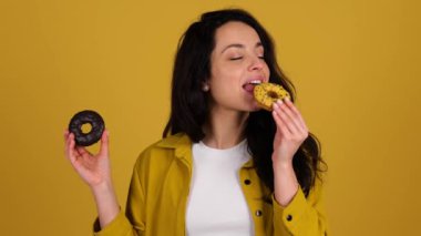 Isırırken çöreğin tadını çıkaran mutlu bir kadın. Sarı arka planda duran kadın. Sağlıklı, abur cubur konsepti. Gerçek zamanlı.