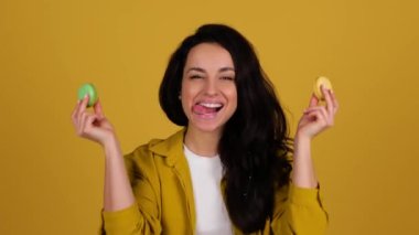 Mutlu genç bayan renkli Fransız kurabiyeleri tutarken eğleniyor. Sarı arka planda duran kadın. Tatlı yemek konsepti. Gerçek zamanlı.