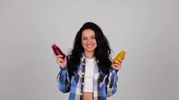 Sonriente Encantadora Hembra Sosteniendo Botellas Jugo Fresco Mientras Posa Estudio — Vídeo de stock
