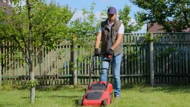 工人在绿色的院子里割草 拿着电动割草机割草的年轻人 花园作业的概念 — 图库视频影像