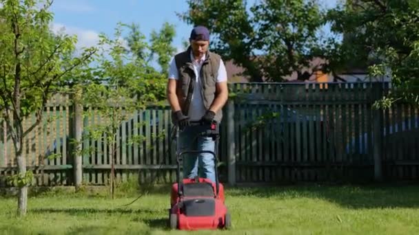 在照料花园和草坪时 拿着割草机的工人走过来 园丁修剪花园 花园作业的概念 — 图库视频影像