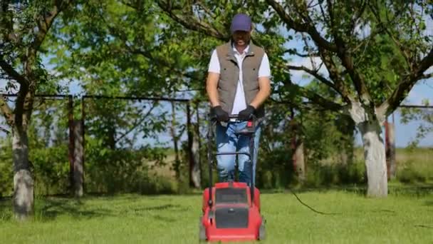 园丁在花园里修剪草坪时使用割草机 戴着帽子和手套工作的人 花园作业的概念 — 图库视频影像