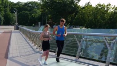 Gülümseyen adam ve kadın, koşudan sonra köprüde dinleniyorlar. Egzersiz, koşu ve spor konsepti. Gerçek zamanlı.
