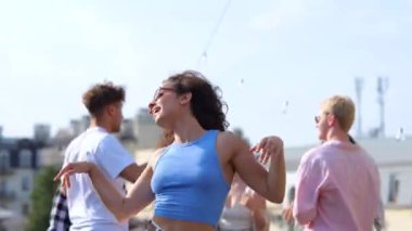 Gamsız, gülümseyen, eğlenen genç bir kadın arka planda arkadaşlarıyla dışarıda terasta dans ederken. Yaşam tarzı, arkadaşlık, eğlence, açık parti konsepti. Gerçek zamanlı.