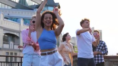 Çatıdaki açık hava partisinde el ele tutuşurken arkadaşlarıyla dans eden genç ve güzel bir bayan. Yaşam tarzı, eğlenceli konsept. Gerçek zamanlı.